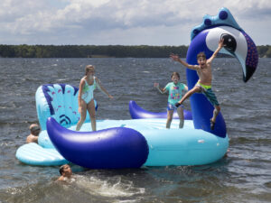 Children jump off a giant inflatable bird into a lake