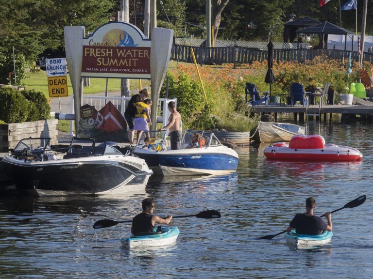 Two kayakers head down stream, close to a sign reading Canada's Fresh Water Summit