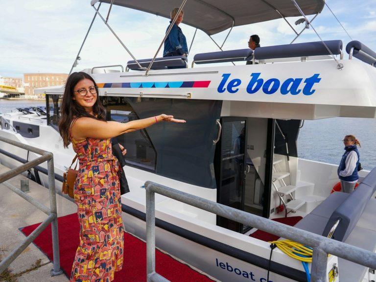 A smiling woman gestures at a Le Boat houseboat