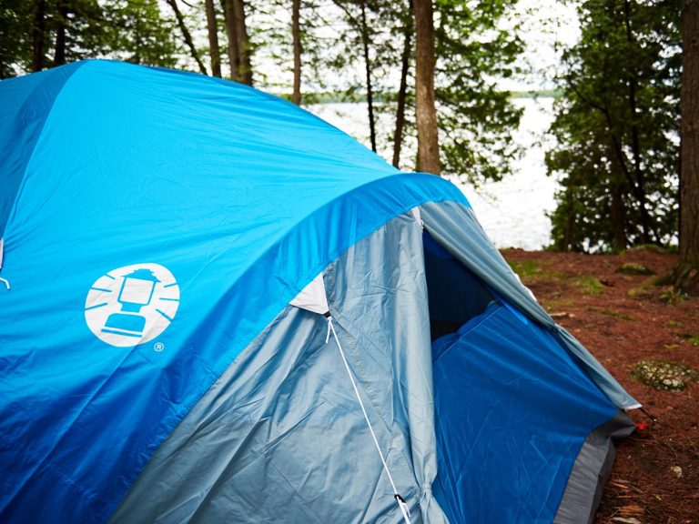 A blue tent, with lake and trees in the background