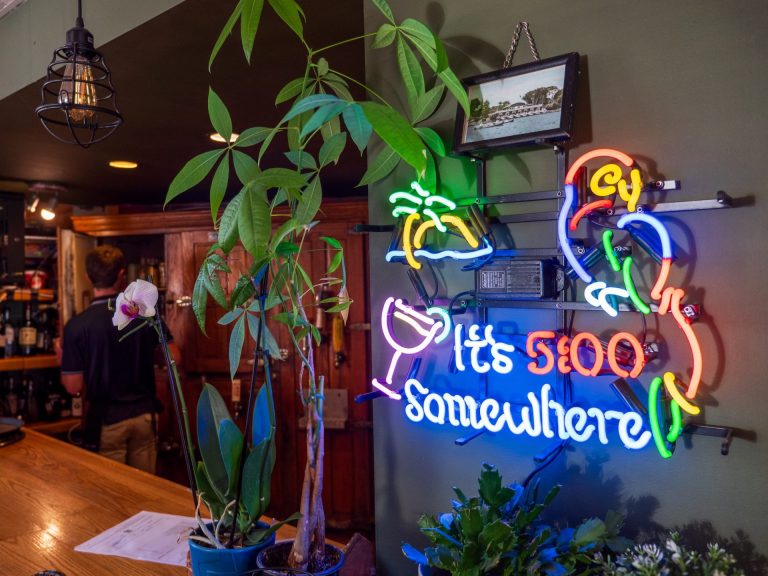 Neon sign reading "It's 5:00 Somewhere," with bar visible to the left