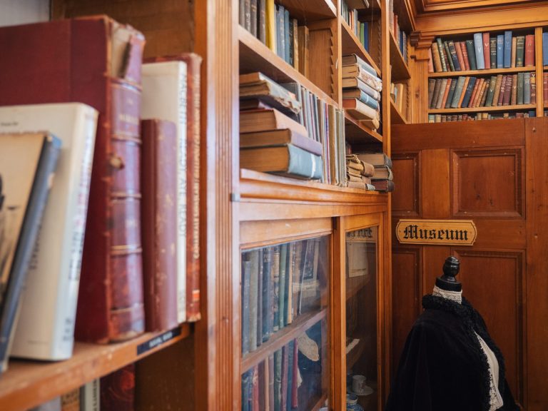 Antique books on a shelf; an open door in the background has a sign reading "Museum"