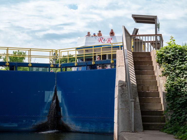 People in a houseboat wait at the top of a lock for the large blue doors to open
