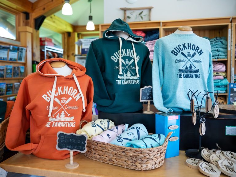A row of three hoodies in orange, green and light blue, all branded "Buckhorn - The Kawarthas"