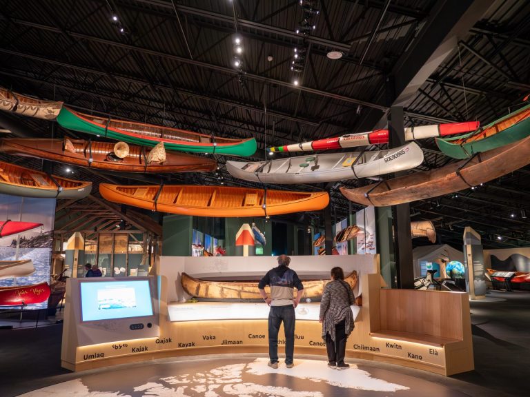 Two people stand looking at a museum display of canoes