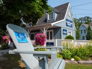 A Muskoka chair in the foreground, Fenelon Falls Tourist Info Centre in the background, with gardens and hanging flowerpots creating a colourful atmosphere
