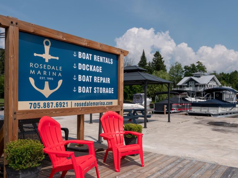 A sign reading Rosedale Marina with red Muskoka chairs underneath