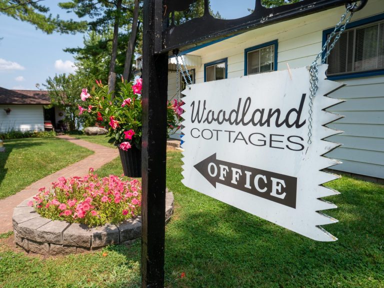Sign reading Woodland Cottages Office points towards sunny, well manicured path