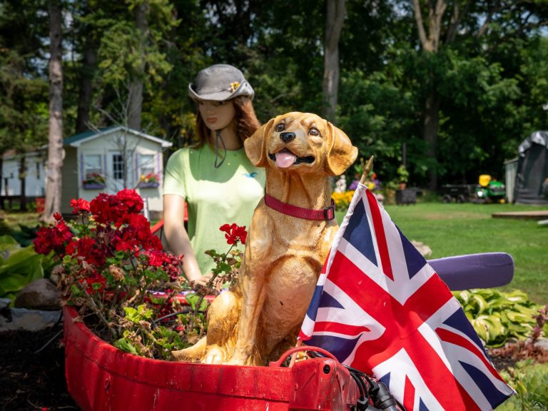 A canoe turned into a flowerbox, with a Union Jack flag, statue of a golden retriever, and mannikin in a hat