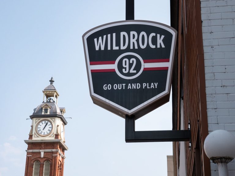Sign reading Wild Rock 82 — Go Out and Play, with clocktower in the background