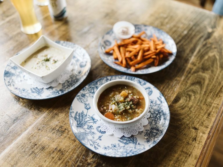 Two bowls of soup and a plate of sweet potato fries, served on decorative dishware