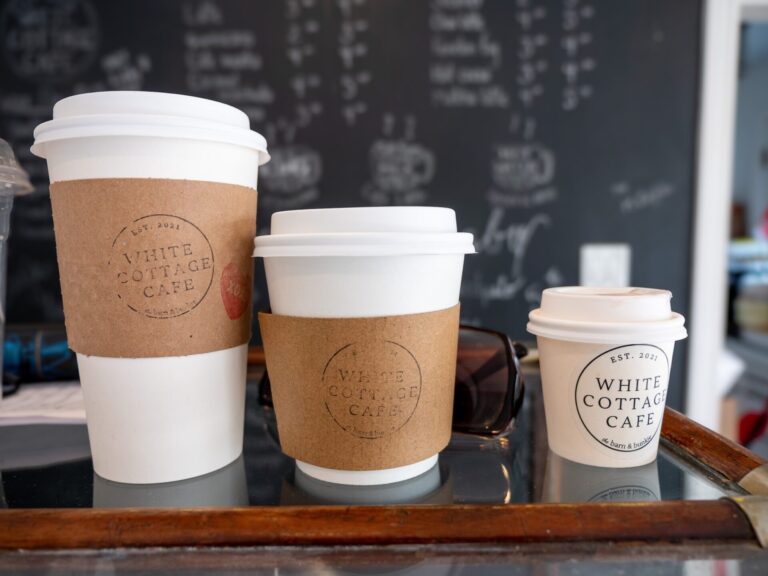 A row of takeout coffee cups branded with White Cottage Cafe on the sleeve