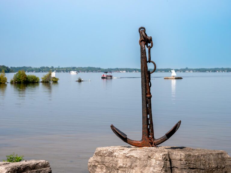 A decorative anchor positioned in front of a lake on a bright blue day