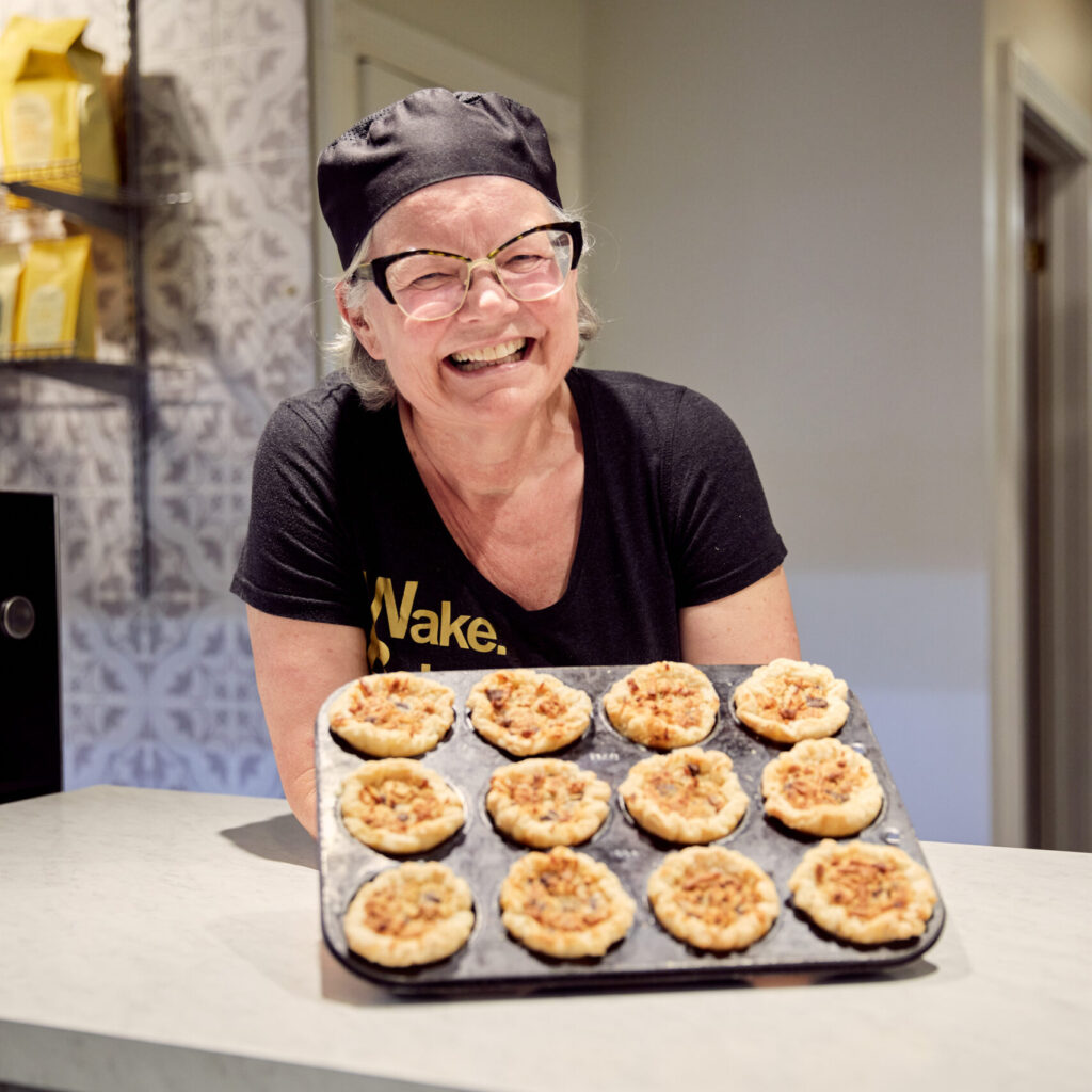 A smiling baker holds out a tray of fresh-baked butter tarts